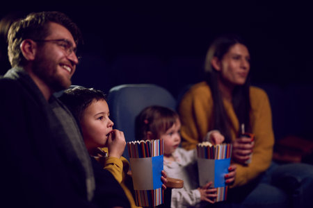 A modern family enjoys quality time together at the cinema, indulging in popcorn while watching a movie with their childrenの写真素材