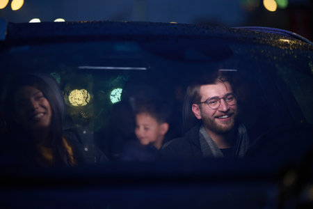 In the nighttime hours, a happy family enjoys playful moments together inside a car as they journey on a nocturnal road trip, illuminated by the glow of headlights and filled with laughter and joyの写真素材