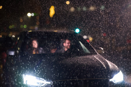 In the midst of a nighttime journey, a happy family enjoys playful moments inside a car as they travel through rainy weather, illuminated by the glow of headlights, laughter, and bondingの写真素材