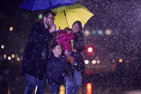 In the midst of a rainy urban night, a happy couple takes their children on a stroll through the city streets, heading towards the cinema for a delightful family movie outingの写真素材