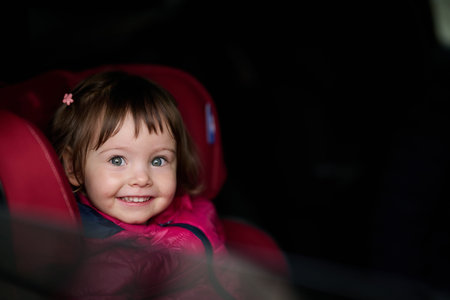 A young girl sits comfortably in a modern car seat, secured and ready for a family adventure on the...