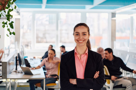 Portrait of young smiling business woman in creative open space coworking startup office. Successful businesswoman standing in office with copyspace. Coworkers working in backgroundの写真素材