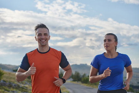 A couple dressed in sportswear runs along a scenic road during an early morning workout, enjoying the fresh air and maintaining a healthy lifestyleの写真素材