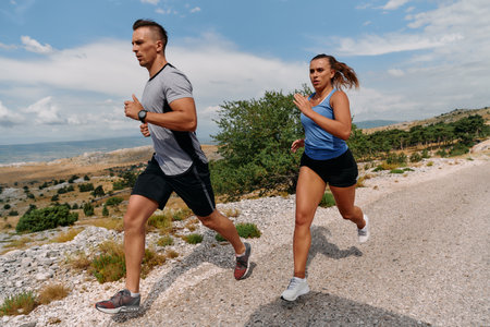 A couple dressed in sportswear runs along a scenic road during an early morning workout, enjoying the fresh air and maintaining a healthy lifestyleの写真素材