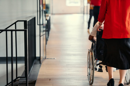 A businesswoman assists her colleague in a wheelchair as they navigate the sleek hallways of a modern startup office, embodying inclusivity and teamworkの写真素材