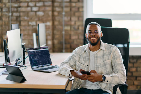 African American entrepreneur takes a break in a modern office, using a smartphone to browse social media, capturing a moment of digital connectivity and relaxation amidst his business endeavors.の写真素材