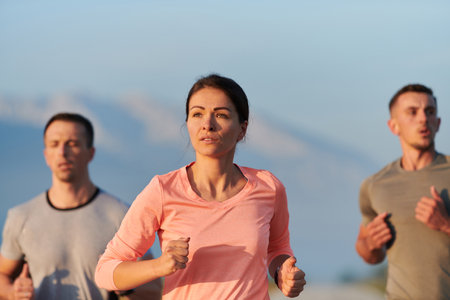 A group of friends, athletes, and joggers embrace the early morning hours as they run through the misty dawn, energized by the rising sun and surrounded by the tranquil beauty of natureの写真素材