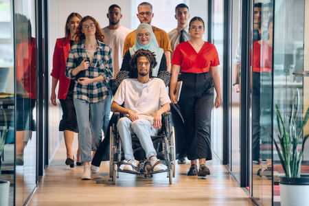 A diverse group of young business people congregates within a modern startups glass-enclosed office, featuring inclusivity with a person in a wheelchair, an African American young man, and a hijab muslim woman .の写真素材