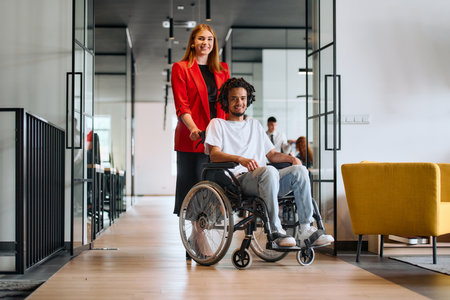A business leader with her colleague, an African-American businessman who is a disabled person, pass by their colleagues who work in modern officesの写真素材