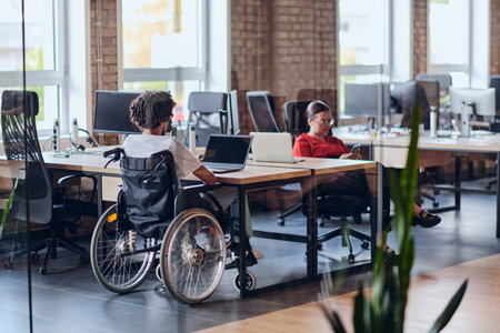 Business colleagues work within a modern startup coworking office, with one of them, an African America in a wheelchair, actively engaging with computers and laptops to collaboratively address various business challenges.の写真素材