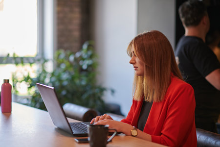 In a contemporary office setting, a young businesswoman is focused on her laptop, displaying dedication and efficiency in her workの写真素材