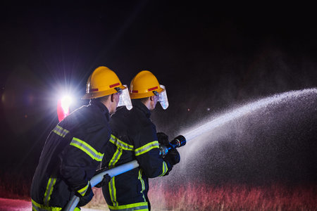 Firefighters using a water hose to eliminate a fire hazard. Team of female and male firemen in dangerous rescue mission.の写真素材