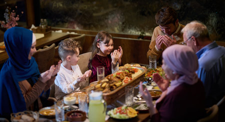 In a modern restaurant setting, a European Islamic family comes together for iftar during Ramadan, engaging in prayer before the meal, uniting tradition and contemporary practices in a celebration of faith and familyの写真素材