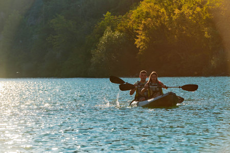 A young couple enjoying an idyllic kayak ride in the middle of a beautiful river surrounded by forest greenery in sunset timeの写真素材