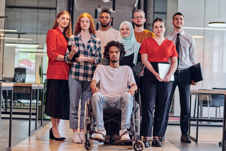 A diverse group of young business people congregates within a modern startups glass-enclosed office, featuring inclusivity with a person in a wheelchair, an African American young man , and a hijab-clad woman, showcasing a dynamic blend of innovation and unity.の写真素材