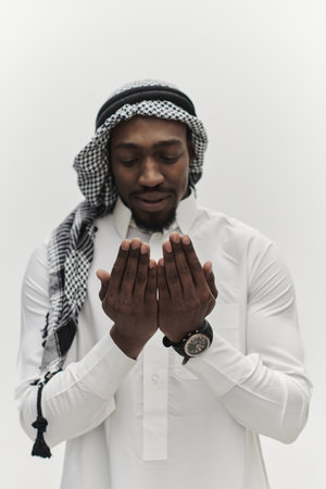 African American Muslim man raises his hands in prayer, seeking solace and devotion to God, as he stands isolated against a serene white backdrop, symbolizing a profound expression of faith and contemplationの写真素材