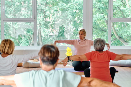 A group of senior women engage in various yoga exercises, including neck, back, and leg stretches, under the guidance of a trainer in a sunlit space, promoting well-being and harmonyの写真素材