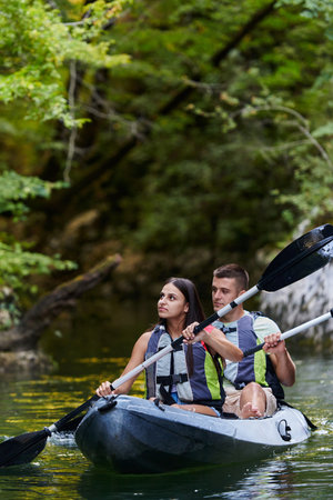 A young couple enjoying an idyllic kayak ride in the middle of a beautiful river surrounded by forest greeneryの写真素材