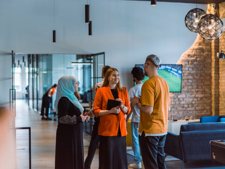 A group of young business colleagues, including a woman in a hijab, stands united in the modern corridor of a spacious startup coworking center, representing diversity and collaborative spiritの写真素材