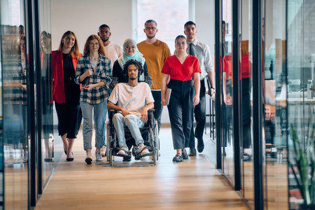 A diverse group of young business people congregates within a modern startups glass-enclosed office, featuring inclusivity with a person in a wheelchair, an African American young man, and a hijab muslim woman .の写真素材