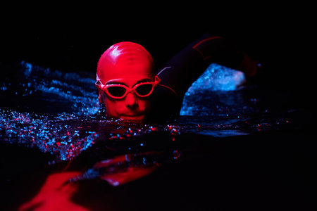 authentic triathlete swimmer having a break during hard training on night neon gel lightの写真素材