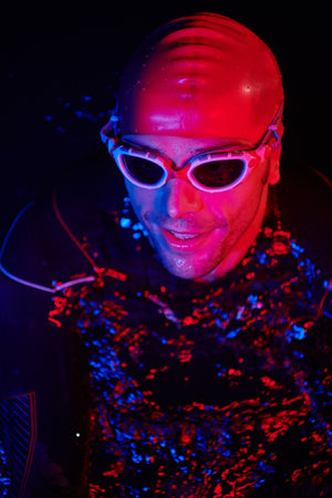 authentic triathlete swimmer having a break during hard training on night neon gel lightの写真素材