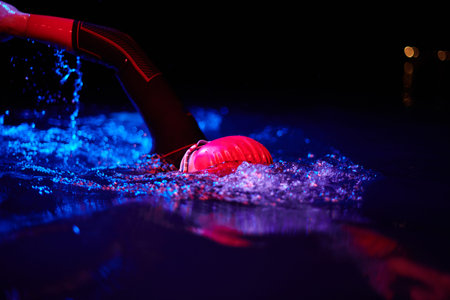 Authentic triathlete swimmer having a break during hard training on night neon gel light