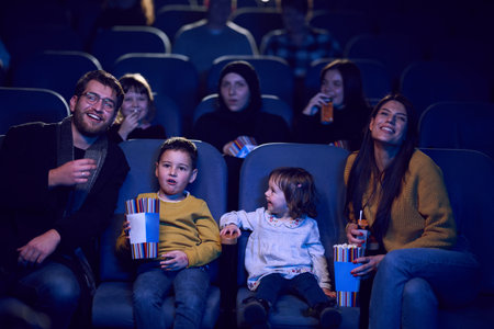 A modern family enjoys quality time together at the cinema, indulging in popcorn while watching a movie with their childrenの写真素材