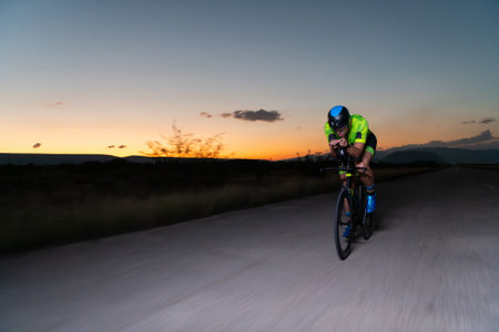 A triathlete rides his bike in the darkness of night, pushing himself to prepare for a marathon. The contrast between the darkness and the light of his bike creates a sense of drama and highlights the athletes determination and perseverance.の写真素材