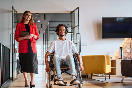 A business leader with her colleague, an African-American businessman who is a disabled person, pass by their colleagues who work in modern officesの写真素材