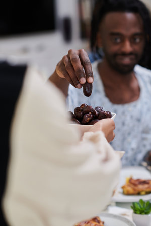 African American Muslim man delicately takes dates to break his fast during the Ramadan month, seated at the family dinner table, embodying a scene of spiritual reflection, cultural tradition, and the shared anticipation of the communal iftarの写真素材