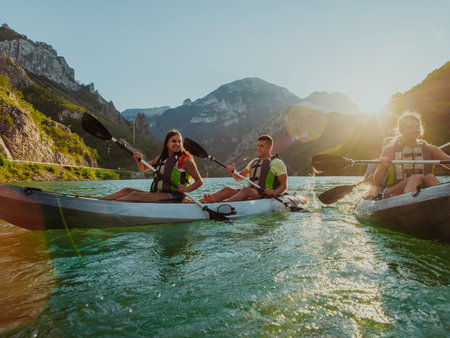 A group of friends enjoying fun and kayaking exploring the calm river, surrounding forest and large natural river canyons during an idyllic sunset.の写真素材