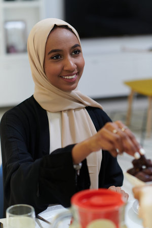 A young Muslim woman adorned in a hijab delicately takes dates, symbolizing the break of her fast in...