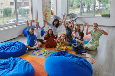 A happy female teacher sitting and playing hand games with a group of little schoolchildrenの写真素材