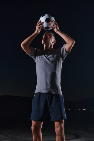 Portrait of a young handsome soccer player man on a street playing with a football ballの写真素材