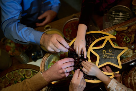 In this modern portrayal, a European Islamic family partakes in the tradition of breaking their Ramadan fast with dates, symbolizing unity, cultural heritage, and spiritual observance during the holy month of Ramadan.の写真素材