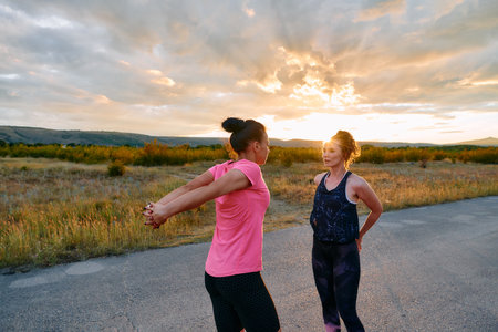 Two Women Athletes Stretching at Sunset in Beautiful Natural Surroundingsの写真素材