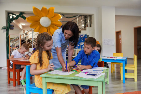 Creative kids during an art class in a daycare center or elementary school classroom drawing with female teacher.の写真素材
