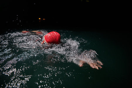 A determined professional triathlete undergoes rigorous night time training in cold waters, showcasing dedication and resilience in preparation for an upcoming triathlon swim competition.の写真素材