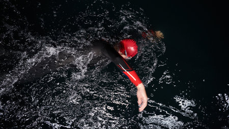 A determined professional triathlete undergoes rigorous night time training in cold waters, showcasing dedication and resilience in preparation for an upcoming triathlon swim competition.の写真素材