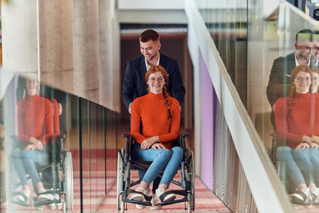 A company director assists his business colleague in a wheelchair, helping her navigate to their startup office, where they work alongside their diverse team of colleagues, emphasizing inclusivity and support in the workplace.の写真素材
