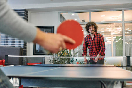 Business colleagues take a break from work to enjoy a game of table tennis, fostering teamwork and camaraderie in the workplaceの写真素材