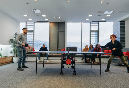Business colleagues take a break from work to enjoy a game of table tennis, fostering teamwork and...