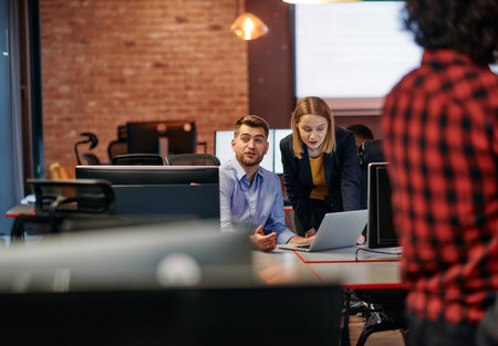 Business colleagues, a man and a woman, engage in discussing business strategies while attentively gazing at a computer monitor, epitomizing collaboration and innovationの写真素材