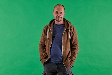 Middle aged bald man in casual attireposes confidently against a green studio backdrop.