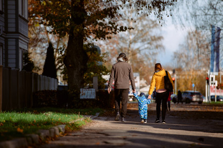 A loving couple strolls through a sunlit park with their young son, surrounded by the vibrant colors of autumn, enjoying a joyful and peaceful family moment together.の写真素材