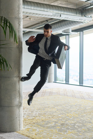 A businessman ecstatically jumping in a modern office, holding a briefcase in his hands, celebrating a moment of success and triumph.の写真素材