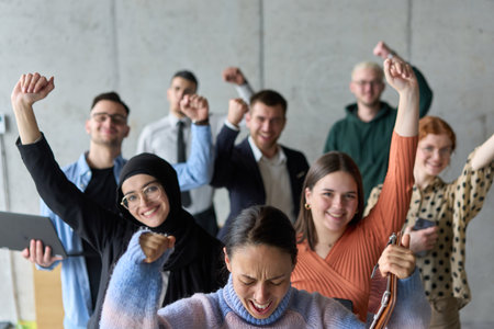 A diverse team of business professionals ecstatically celebrating their success in a modern office, expressing triumph and unity after achieving their goalsの写真素材