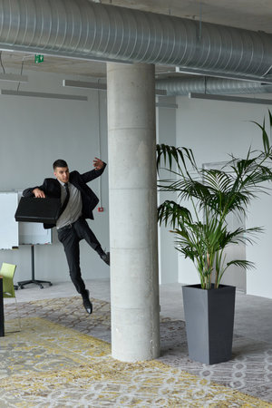 A businessman ecstatically jumping in a modern office, holding a briefcase in his hands, celebrating a moment of success and triumph.の写真素材