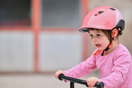 A little girl, dressed in a cute outfit and wearing a helmet, learning to ride her bike for the first time, filled with joy and determination.の写真素材